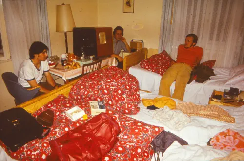 Drei junge Männer in einem vollgestellten kleinem Zimmer