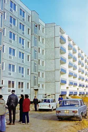 Sechsstöckige Neubau-Platten-Hochhäuser, davor einige Menschen und Autos
